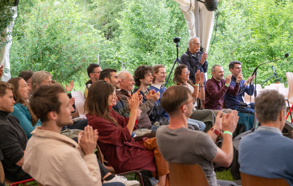 Mehrere Menschen sitzen als Publikum bei einer Veranstaltung in einem Zelt