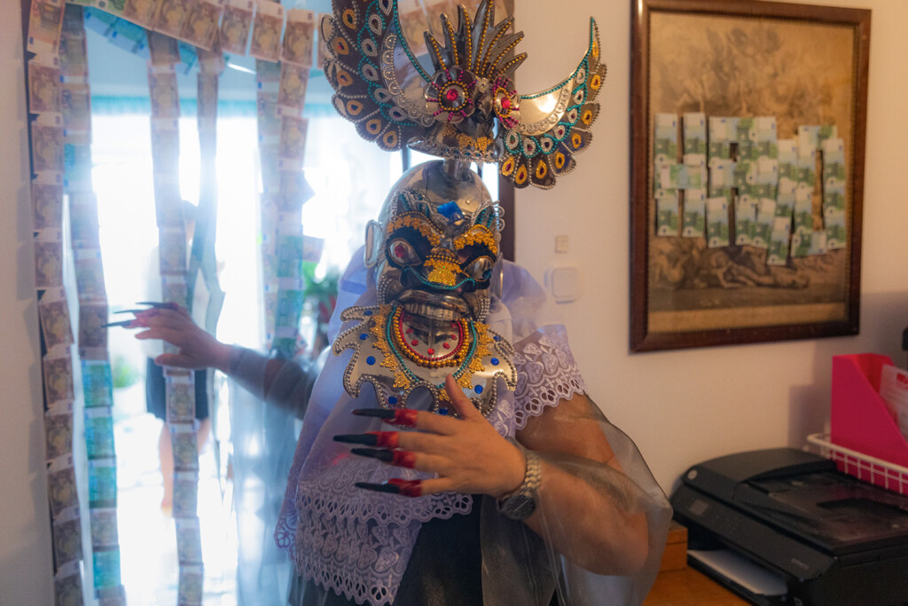 Eine Person mit traditioneller Maske steht in einer Wohnung